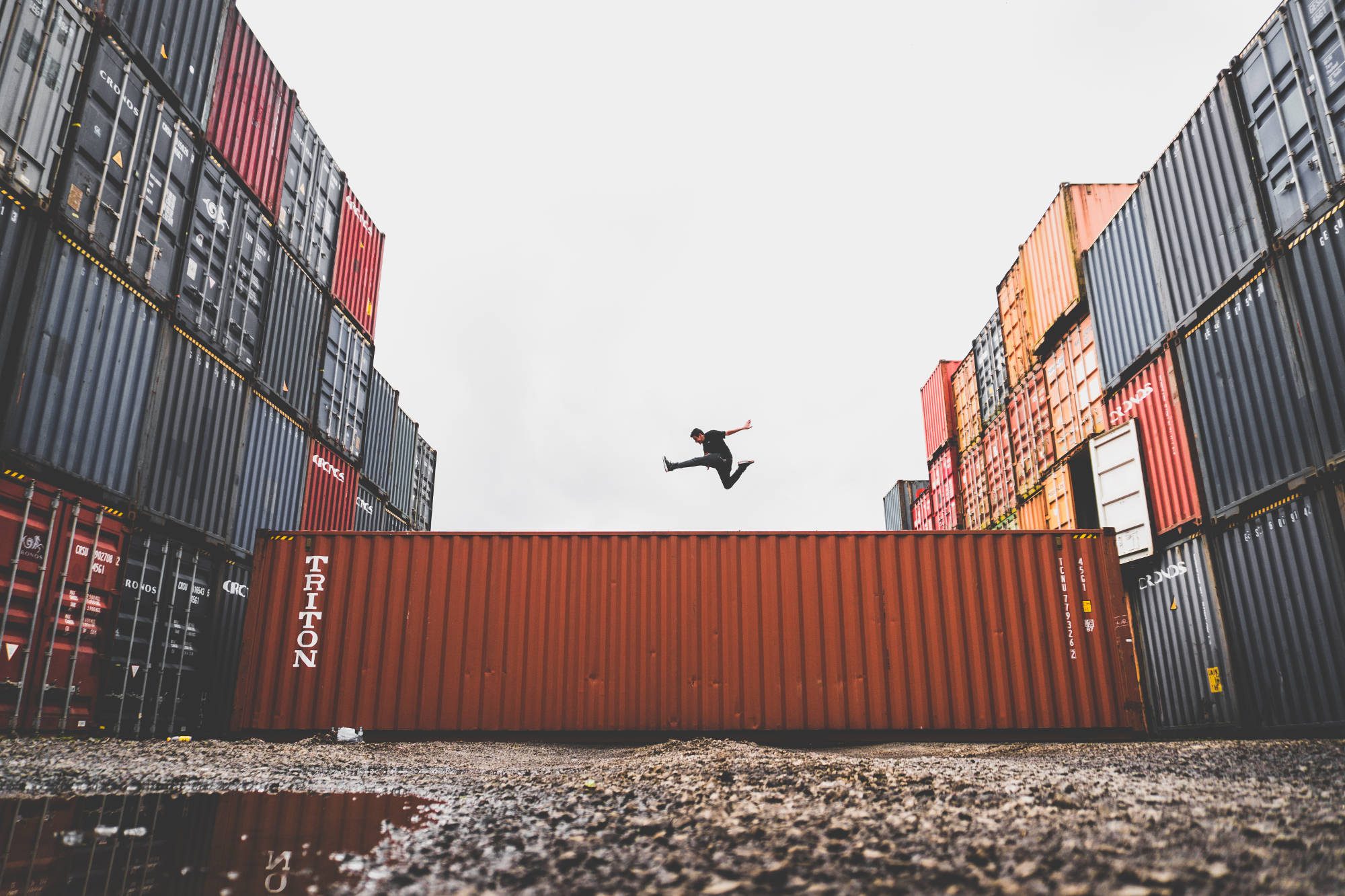 containers stacked in a port, with a man jumping over one of them that is lying across the ground