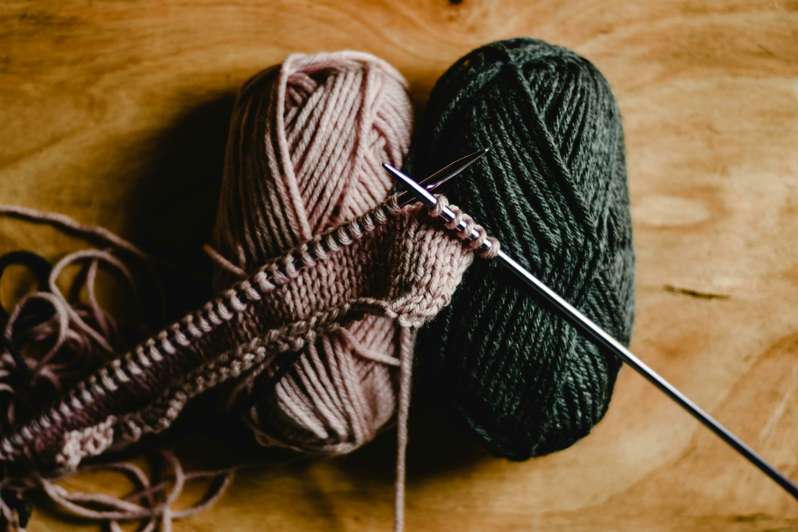 two balls of pink and green wool lying there, and a piece of knitting in progress on two needles